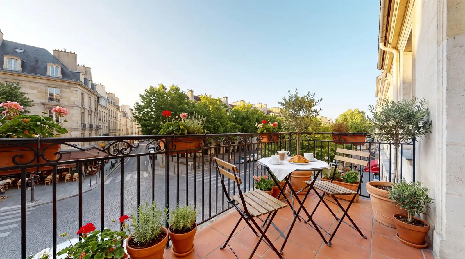 Stadtbalkon einer Altbauwohnung mit Bistrotisch, Geranien und Blick auf eine Boulevard-Kreuzung — KI-generierte Beispielaufnahme